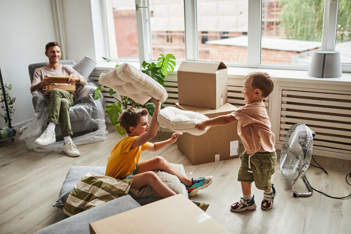 pillow-fight-in-new-home - wecleantoperfection children having a pillow fight in front of moving boxes in a new home